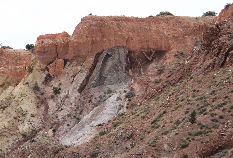 Photograph showing an outcrop of pinkish cliff-forming sandstone and conglomerate overlying slope-forming folded shale (Jurassic) with some sandstone layers.