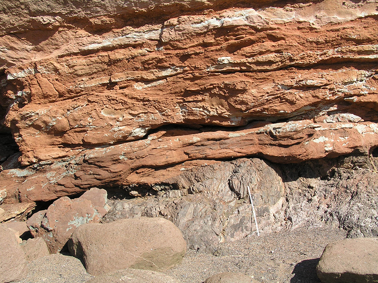 Photograph showing a seaside exposure of an angular unconformity: gently dipping orange layers overlie thin gray layers that are vertical.
