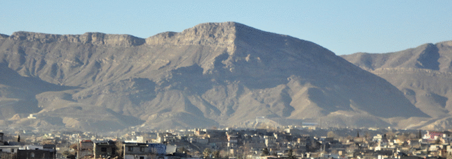 Animated GIF showing an annotated view of a large recumbent fold in the Sierra de Juarez, Mexico. This huge fold makes up the whole upper half of a mountain above a city below. It is very tight, like an alligator mouth opening to the left. The hinge is to the right side of the view. The axial plane (that divides the fold in half) runs horizontally through the middle of the fold. The beds at the crest of the mountain are upright in their orientation, but the layers in the lower half of the mountain have been flipped over into an up-side-down orientation.