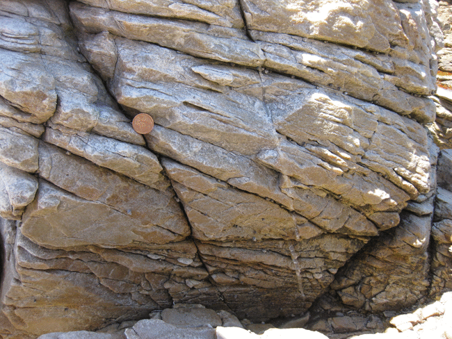 Animated GIF showing annotation of a photograph of up-side-down cross-bedding. One big bed of quartzite is horizontal across the field of view. A penny serves as a sense of scale. The cross-beds are concave-DOWN, with truncated LOWER surfaces and tangential UPPER surfaces. Paleo-"up" is therefore at the BOTTOM of the photo.
