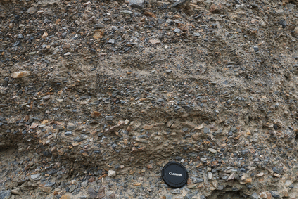 Animated GIF of an annotated photograph showing a layered deposit of gravel. Oblong clasts in the gravel all tilt to the left, an example of imbrication. The implication is that the current flowed from the left toward the right. A lens cap serves as a sense of scale; the field of view is approximately 1 m wide by half a meter tall.