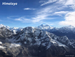 Photograph over rough, snowy mountains. Blue sky with clouds is above. The photo is labeled "Himalaya."