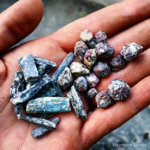 Photograph showing a handful of gravel: a blend of two minerals: bright blue blades of kyanite, and round cranberry-colored garnets.