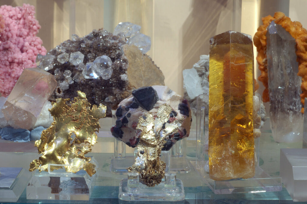 Photograph of a museum display of many well-formed mineral crystals of various sizes, shapes, and colors.