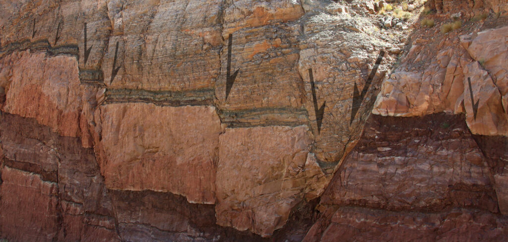 Annotated photo showing a cross-sectional view of some horizontal sedimentary layers, but in seven places, the layers are broken and moved relative to one another along steep fracture surfaces. This produces a "stairstep" pattern of offsets in the sedimentary layers. No scale is provided. Arrows show the downward sense of offset between formerly continuous layers.